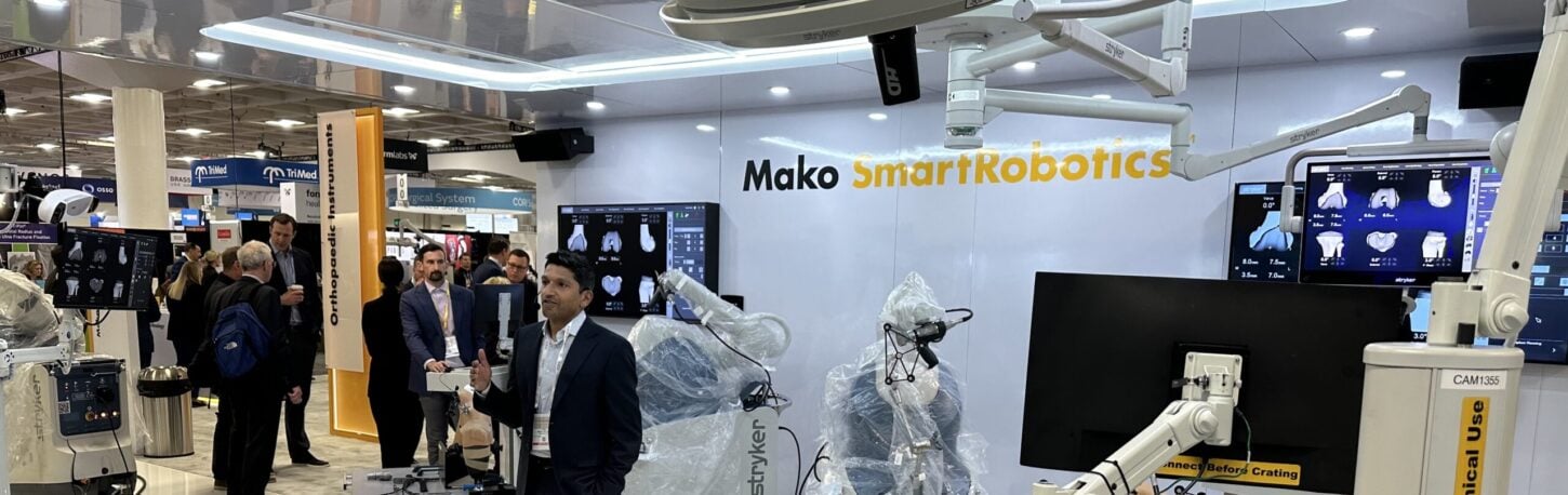 A man standing in front of a robotic total joint replacement machine at a medical conference.