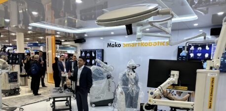 A man standing in front of a robotic total joint replacement machine at a medical conference.