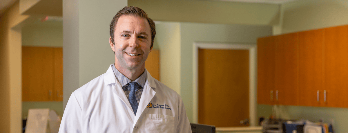 Photo of a doctor smiling holding a medical model of a foot and ankle