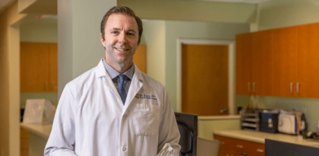 Photo of a doctor smiling holding a medical model of a foot and ankle