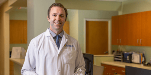 Photo of a doctor smiling holding a medical model of a foot and ankle
