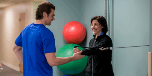 Two people standing in a physical therapy exercise room.